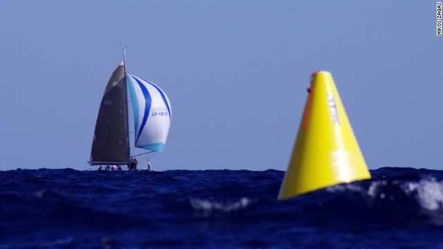 An out-of-focus yellow buoy bobs on the surface of the water as, in a distance, Pachakis Ioannis glides over the water in October's Cretan Union Cup, captured on a Pentax 450mm.