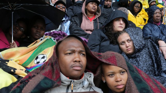 People take shelter under blankets and umbrellas during the memorial service for former South African President Nelson Mandela at FNB Stadium in Johannesburg on Tuesday, December 10. Thousands of South Africans and more than 90 heads of state gathered to honor the revered leader, who died Thursday, December 5. He was 95.