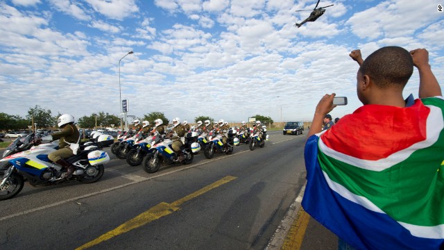 A child draped in the South African flag takes a photo of the procession as the body of Mandela arrives at the Waterkloof air base.