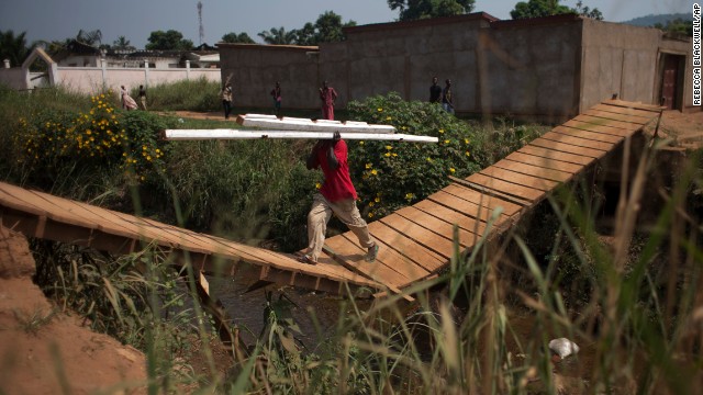 A man carries beams stripped from a house, back left, said to have belonged to a Seleka officer who had been attacking the surrounding Christian population, in Bangui on December 28.