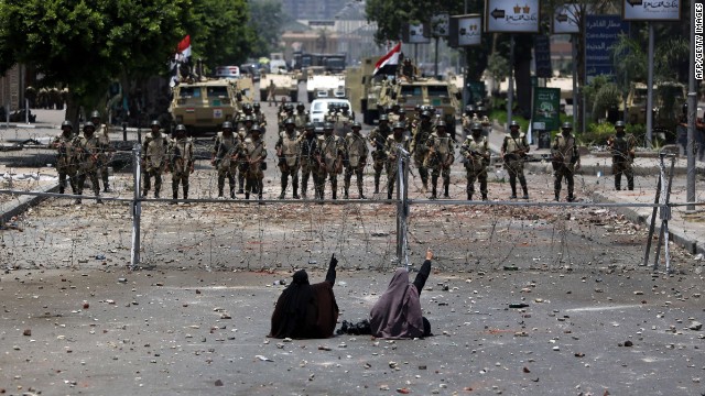 Two veiled Egyptian women, supporters of Mohamed Morsy, sit in front of police standing behind barbed wire fencing that blocks the access to the headquarters of the Republican Guard in Cairo on July 8, 2013. 