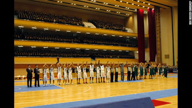 U.S. and North Korean basketball players raise their hands to the crowd after the game.