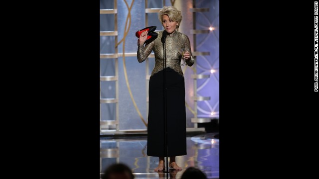 Actress Emma Thompson holds a martini in one hand and her shoes in the other while presenting an award.