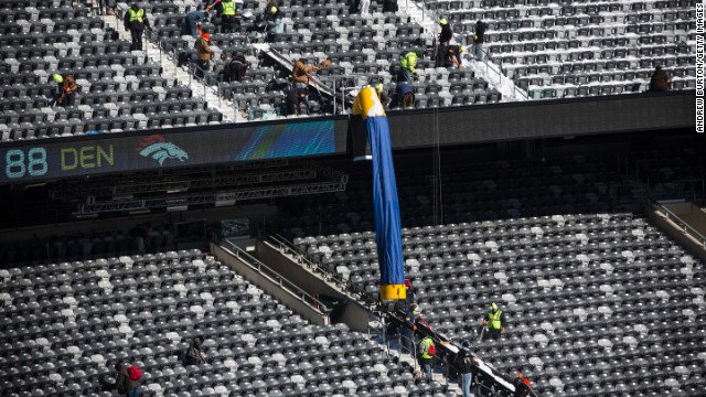 Workers remove snow from the stands. Cold-weather welcome kits have been produced for fans. They will include earmuffs, hats, mittens and lip balm, among other items.