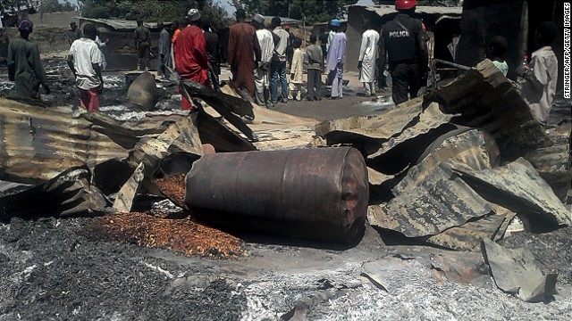 Police officers stand guard in front of the burnt-out remains of buildings in the village of Konduga, Nigeria, on February 12, 2014.