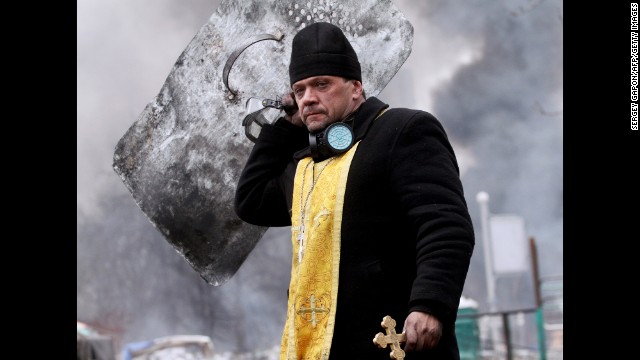 A priest walks with a cross and shield during clashes in central Kiev on February 20.