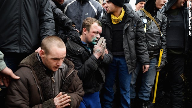 Two pro-government supporters are made to pray February 23 in front of a shrine to dead anti-government protesters.