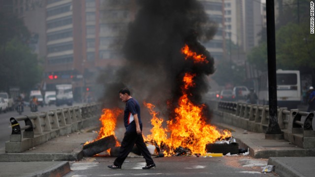 A pedestrian moves past a burning barricade blocking a highway in Caracas on February 24.