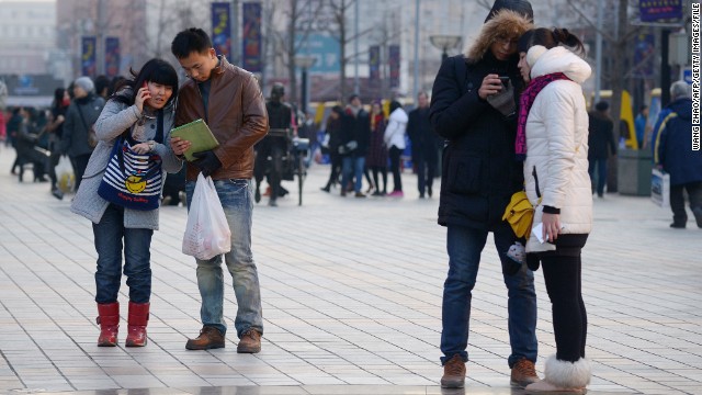 Pedestrians in Beijing use their mobile phones as they wait to cross the street.