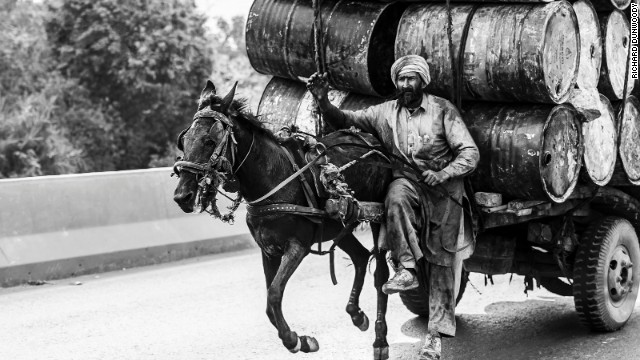A man drives his horse at full tilt down a dual carriageway with a large load of empty water barrels in Faisalabad, Pakistan.