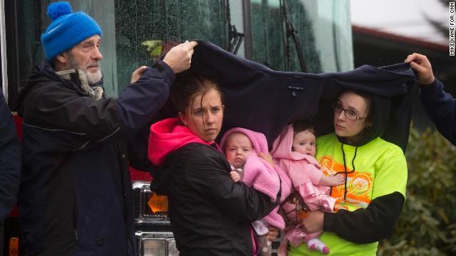 Ralph Jones helps provide shelter for Brooke Odenius, right, Klarissa Calviste and their baby daughters during the moment of silence at the fire house in Darrington.