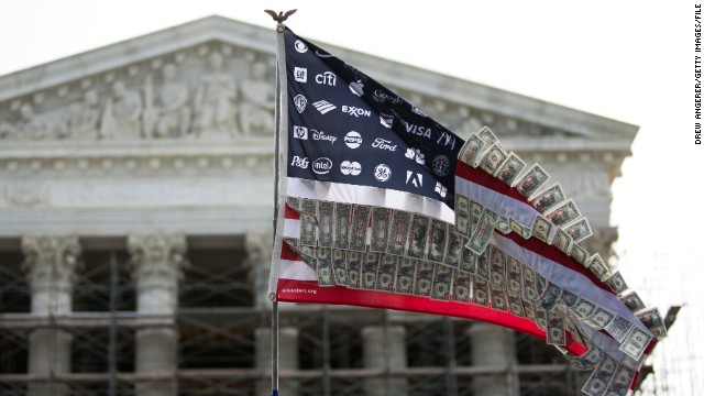 A flag adorned with corporate logos and fake money flies at a rally against money in politics in front of the Supreme Court.