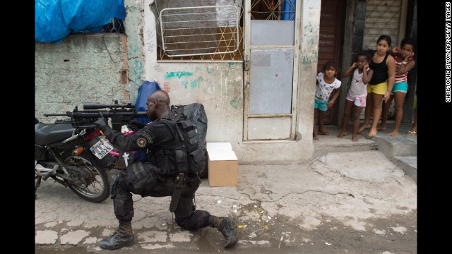 Girls watch a paramilitary police sniper secure an area in the favela as Brazilian soldiers conduct a search for weapons. The shantytown is just a few kilometers from Rio's international airport, where many of the expected 600,000 international fans will land.