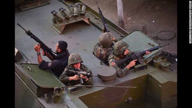 Police and military personnel watch from the rear hatch of an armored personnel vehicle during a street patrol along the Nueva Holanda favela, part of the Complexo da Mare.