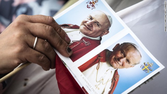 A card shows portraits of John XXIII, left, and John Paul II as pilgrims wait for the canonization ceremony to begin.