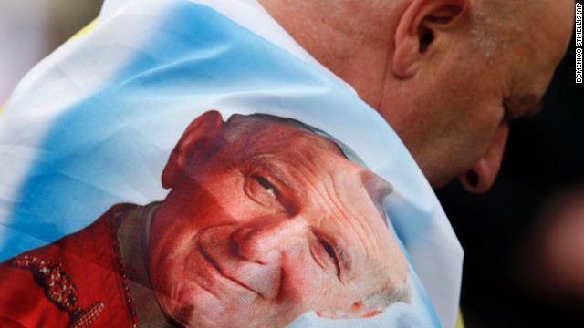 A man is wrapped in a flag bearing a picture of Pope John Paul II in St. Peter's Square.