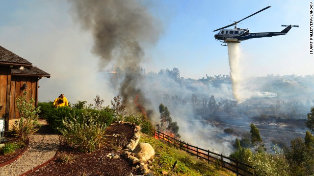 A helicopter drops water near the Rancho Santa Fe neighborhood of San Diego on Tuesday, May 13. A wildfire forced the evacuation of more than 20,000 homes in Southern California, officials said, as a high-pressure system brought unseasonable heat and gusty winds to the parched state.