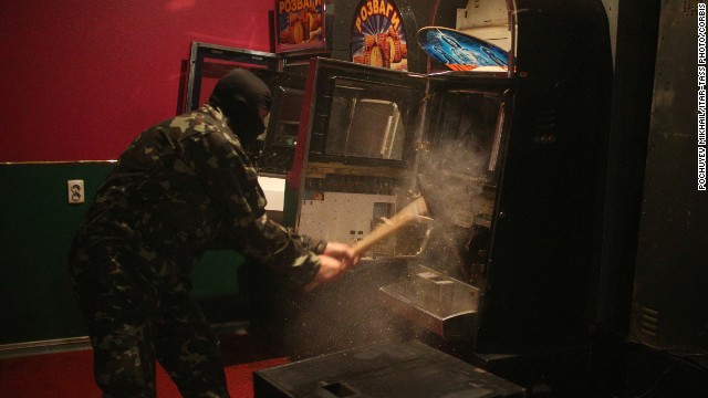 A member of a "self-defense" squad smashes a slot machine with a sledgehammer Monday, May 12, at an illegal club in Slovyansk.