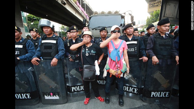 Two protesters stand in front riot police during an anti-coup demonstration in Bangkok on Monday, May 26. Demonstrators have taken to the streets in opposition to the coup, while some Thais express hope the military will bring an end to the political crisis.