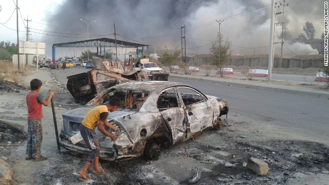 Children stand next to a burnt vehicle during clashes between Iraqi security forces and ISIS militants in Mosul on Tuesday, June 10.