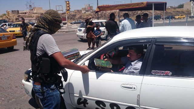 An ISIS member distributes a copy of the Quran, Islam's holy book, to a driver in Mosul on June 22. 