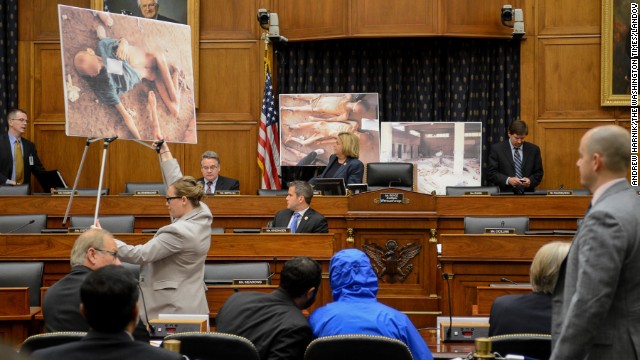 Photographs of victims of the Bashar al-Assad regime are displayed as a Syrian Army defector known as "Caesar," center, appears in disguise to speak before the House Foreign Affairs Committee in Washington. The briefing on Thursday, July 31, was called "Assad's Killing Machine Exposed: Implications for U.S. Policy." Caesar was apparently a witness to al-Assad's brutality and has smuggled more than 50,000 photographs depicting the torture and execution of more than 10,000 dissidents. 