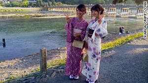 Kimono-clad Japanese tourists pose in front of Arashiyama\'s Togetsukyo Bridge. 