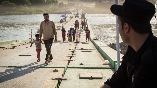 A Kurdish border guard watches while people cross. 