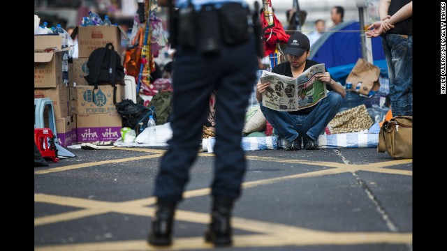 A pro-democracy protester reads a newspaper in Hong Kong's Mong Kok district on Tuesday, October 7, as a police officer stands nearby.