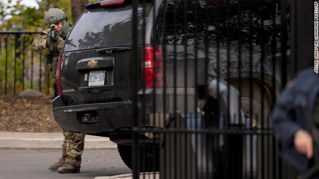 A heavily armed officer takes position at the gate of 24 Sussex Drive, the official residence of Canadian Prime Minister Stephen Harper. Harper was evacuated from the Parliament building and is safe, his press secretary tweeted.