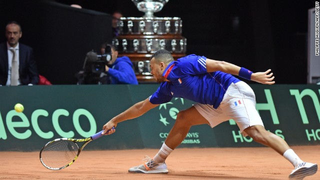 With the giant Davis Cup trophy behind him, Tsonga stretches to retrieve a shot in going down to Wawrinka
