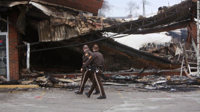 Police officers walk past the smoldering remains of a beauty supply store on November 25.