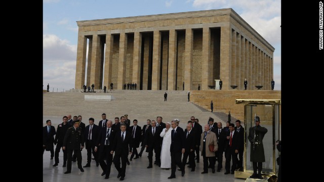 The Pope, surrounded by security and officials, walks the grounds of the mausoleum November 28.