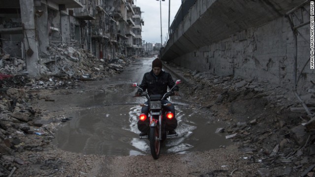 A man drives his motorcycle through a puddle in Aleppo on Wednesday, November 26.