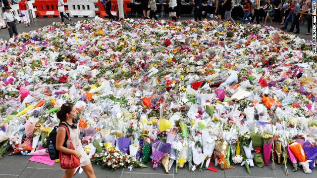 A woman walks past flowers placed by people as a mark of respect for the victims of Martin Place siege on Tuesday, December 16.