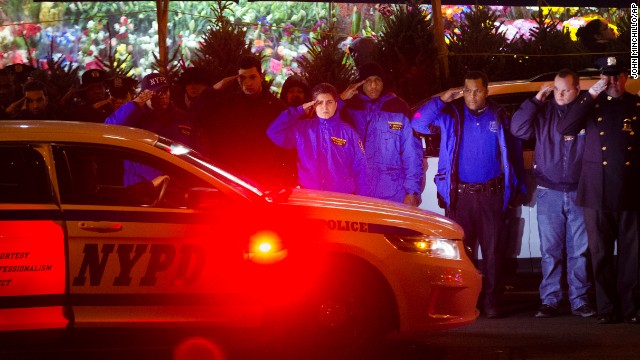 Mourners stand at attention as the bodies of two fallen NYPD officers are transported from Woodhull Medical Center on Saturday, December 20. 