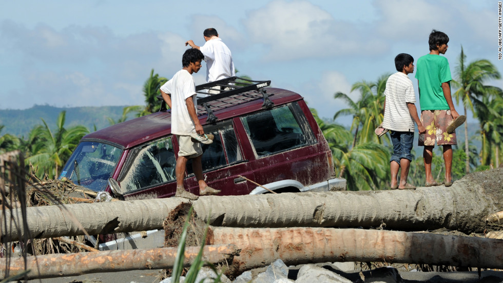 Residents stand next to a vehicle washed up among debris along a river in New Bataan on December 6.