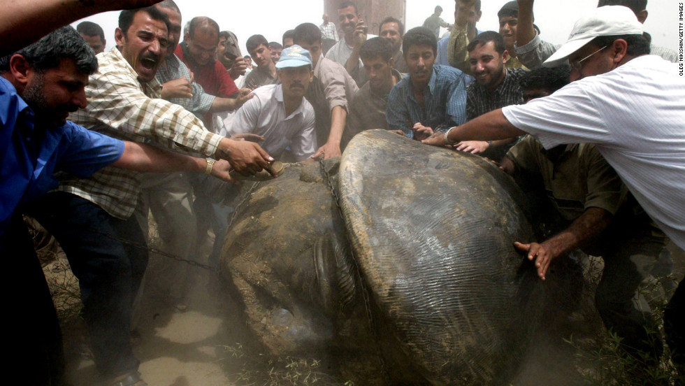 Iraqi men push the head of a statue of Saddam Hussein after its destruction on April 18, 2003, in Baghdad.