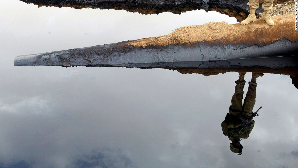 Army Cpl. Curtis Laymon of the 101st Airborne Rakkasan regiment is reflected in a pool of oil from the Iraqi-Turkey pipeline in Iraq's Ninewa province on October 29, 2003. The pipeline was blown apart by saboteurs two weeks earlier.