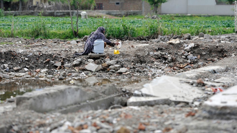 A Pakistani woman fills a container with water at the site of the demolished compound on April 25, 2012.