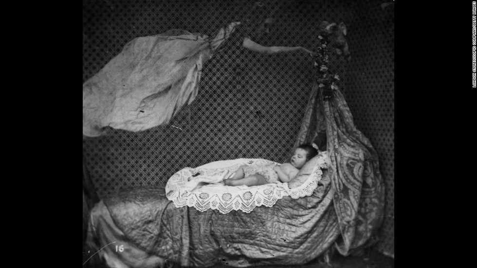 A spectral figure hovers over a sleeping baby in a crib.
