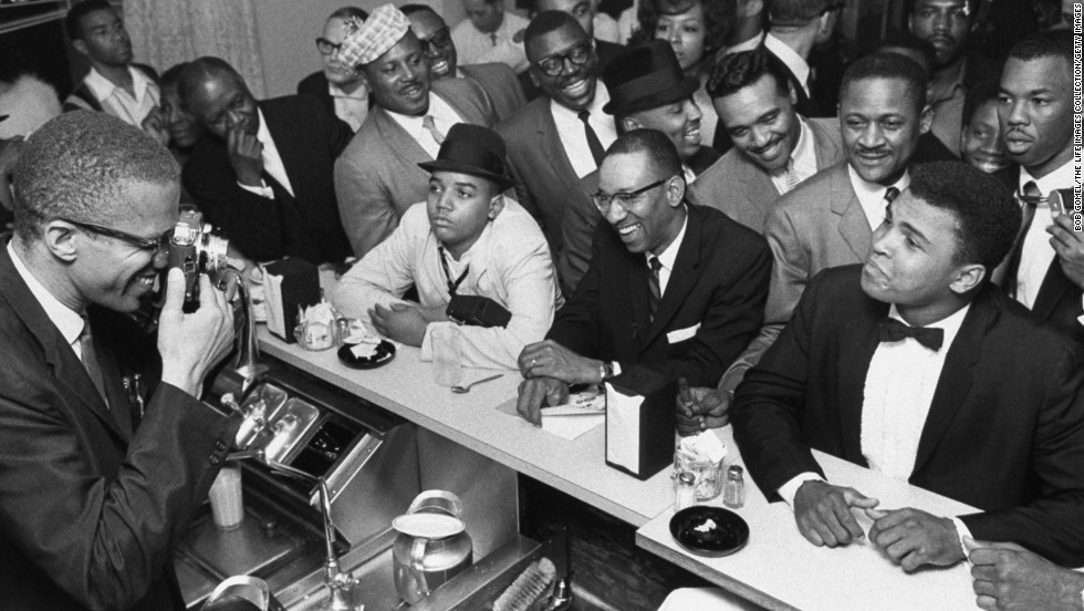 Civil rights activist Malcolm X, left, takes a picture of a tuxedo-clad Ali surrounded by jubilant fans in March 1964. Shortly after the Liston fight, Ali announced that he had joined the Nation of Islam and changed his name from Cassius Clay.