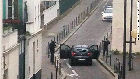 Gunmen face police officers near the offices of French satirical magazine Charlie Hebdo in Paris on Wednesday, January 7. At least 12 people were killed in an attack at the magazine, which had spurred protests in the past over caricatures of the Prophet Mohammed. Its offices were set afire in November 2011.