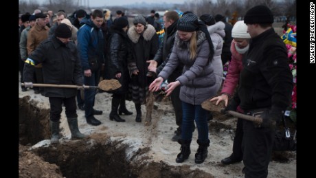 People in Mariupol, Ukraine, pour soil into the grave of a recent shelling victim on Monday, January 26.