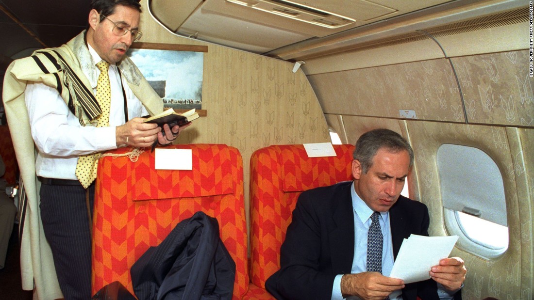 Netanyahu, as Israel's deputy foreign minister, goes through some papers as Government Secretary Elyakim Rubinstein recites morning prayers on a flight from New York to Washington in April 1989.