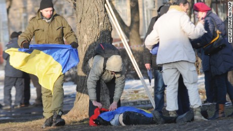 A man holds a Ukrainian flag as he covers a victim of an explosion in Kharkiv, Ukraine, on Sunday, February 22. The explosion during a peaceful protest left two dead and 15 wounded.