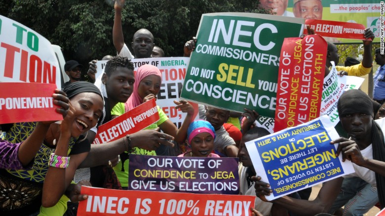 People in Abuja hold signs to protest the postponement of the elections.