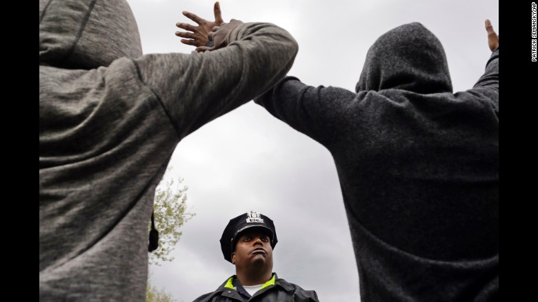 A member of the Baltimore Police Department stands guard outside the Western District station as men hold their hands up in protest on April 22.