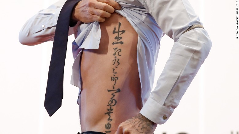 British football player David Beckham shows his tattoo to fans during his visit to Peking University on March 24, 2013 in Beijing.
