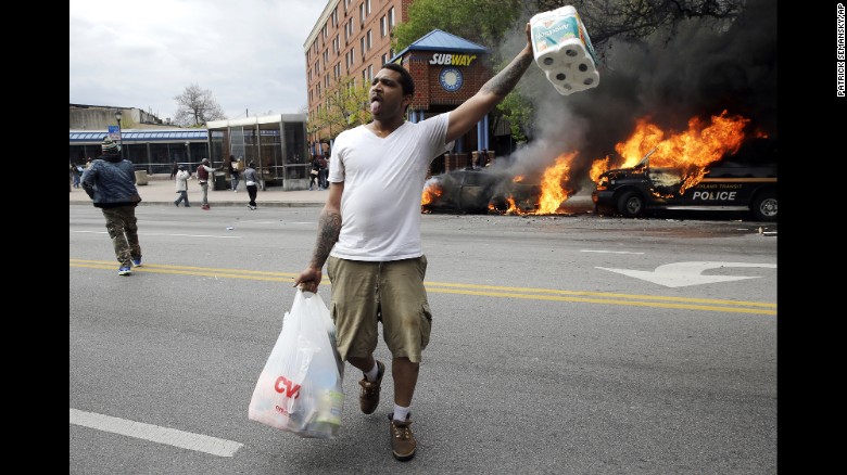 A man carries items from a store as police vehicles burn on April 27.